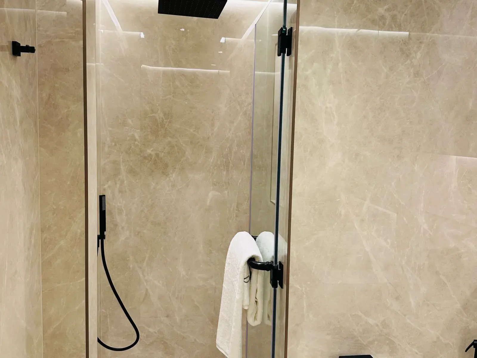 Walk-in shower lined in warm stone behind a frameless glass screen