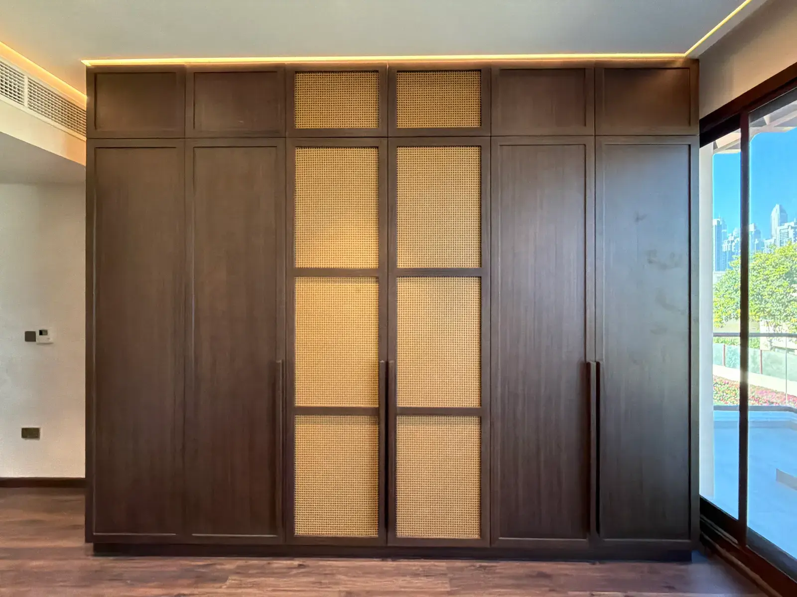 Full-height walnut and cane wardrobe wall in a bedroom