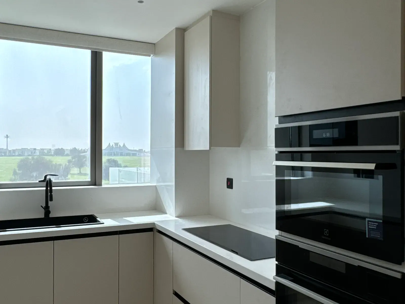 Handleless kitchen in pale gloss with black built-in appliances and a window over the greens