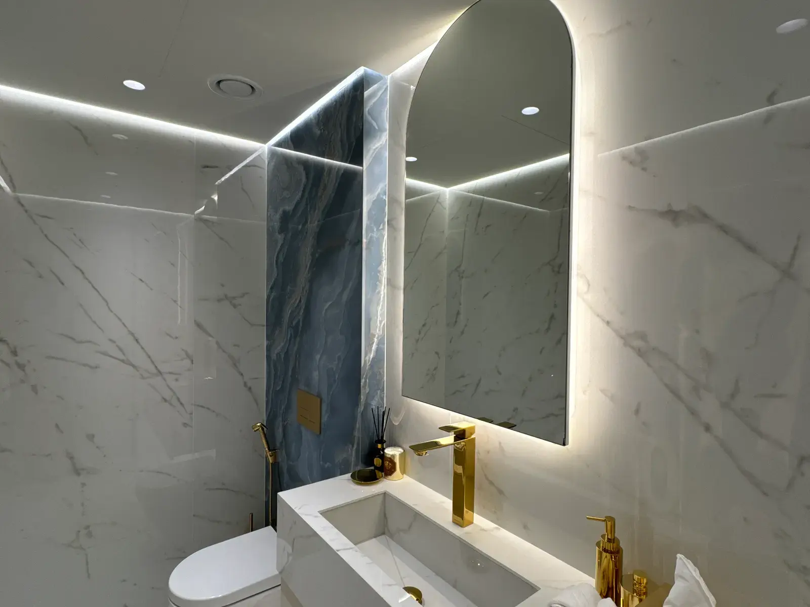 Bathroom in white marble with a blue-grey marble feature panel and gold taps