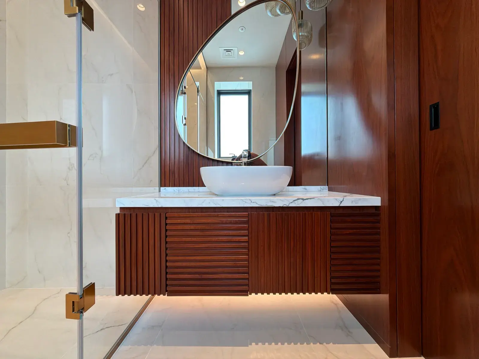 Ribbed mahogany vanity with stone basin and backlit round mirror