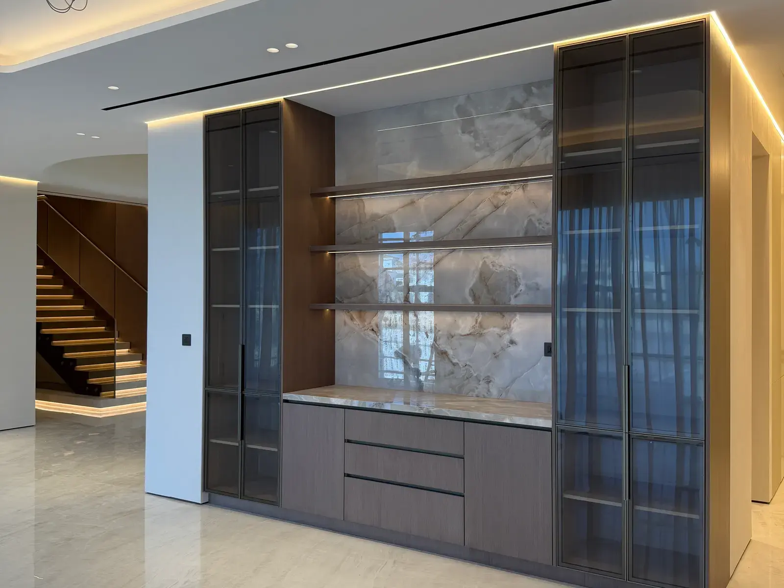Backlit onyx display joinery in bronze-framed glass beside a timber staircase in a Palm Jumeirah villa