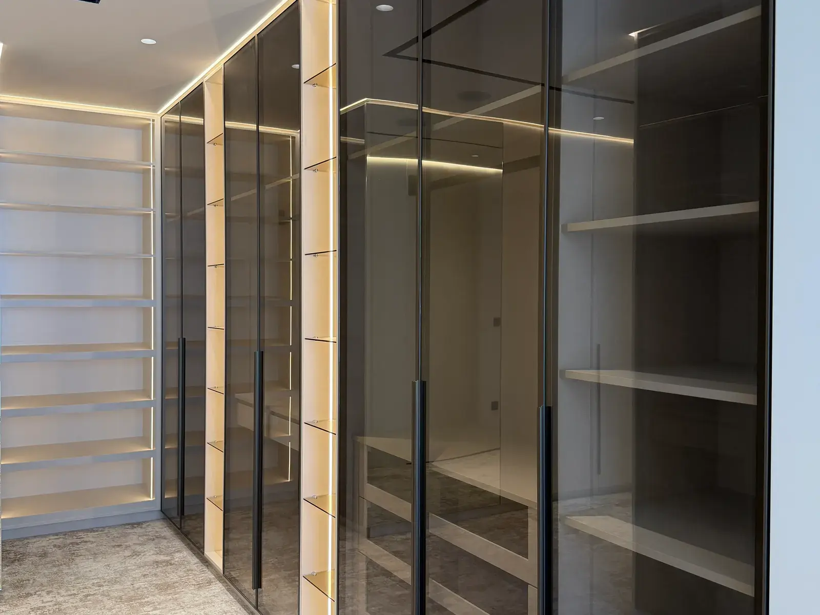 Walk-in wardrobe with bronze-tinted glass doors and internal lighting