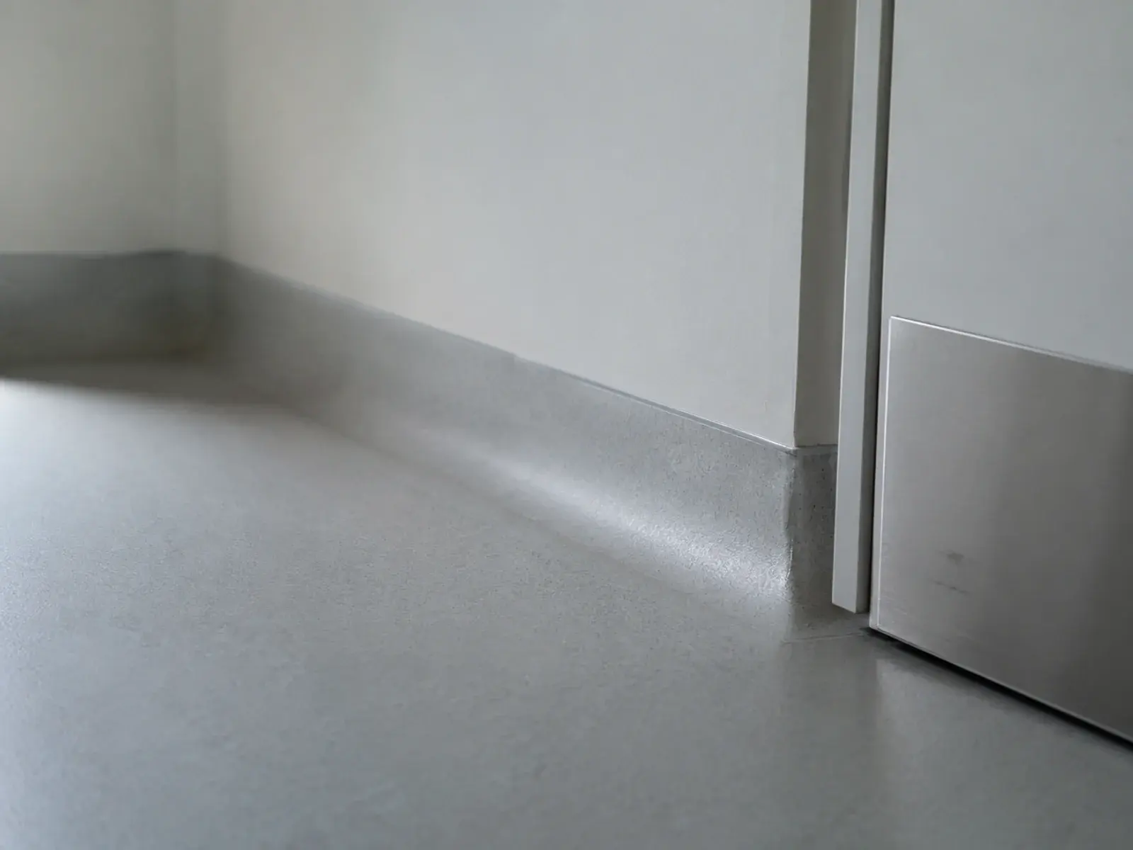 Clinic corner detail showing sealed vinyl flooring carried into a coved skirting and a flush ceiling