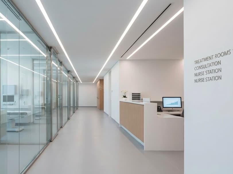 Clinic treatment corridor with recessed linear ceiling lighting and a built-in two-level nurse station