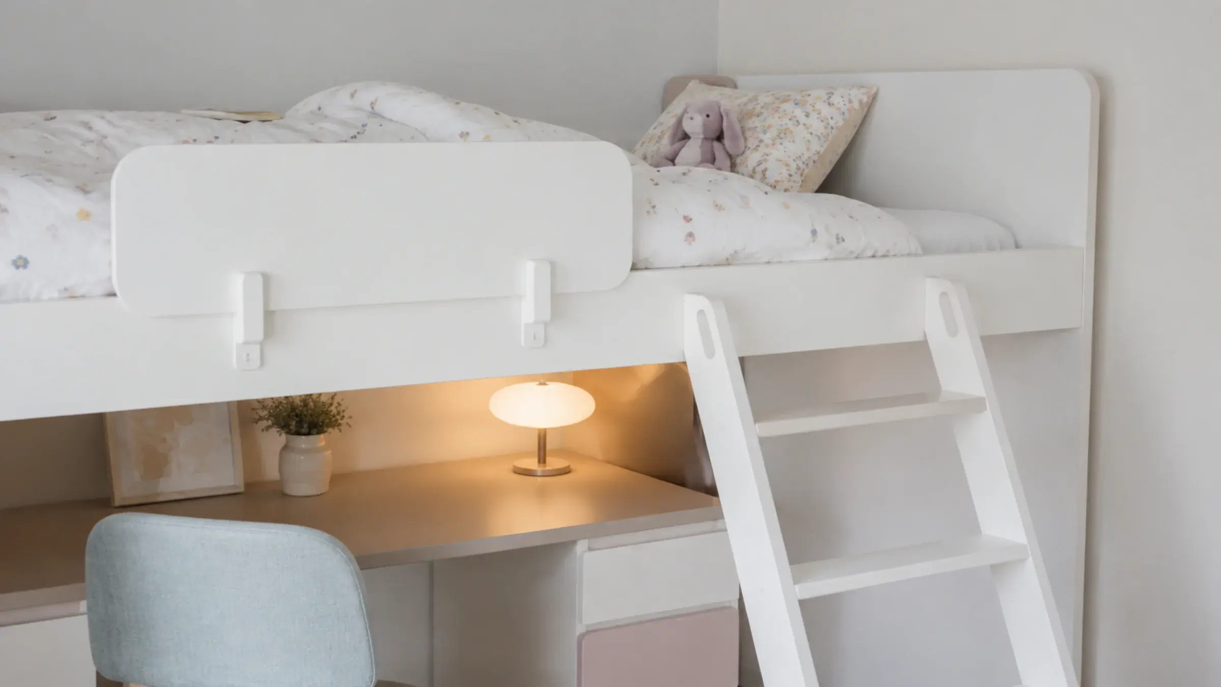 Built-in loft bed with a wide-tread ladder and safety rail in a child-scaled bedroom, a stuffed toy left on the pillow