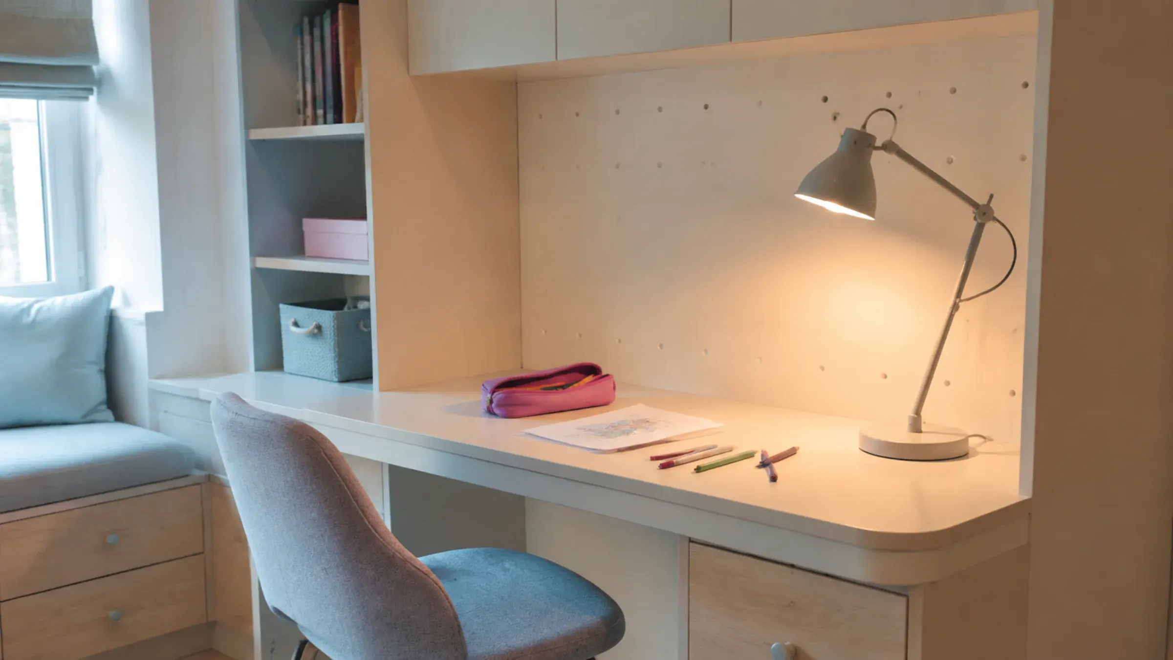 Child-height built-in desk with a rounded front edge and an adjustable task lamp, a pencil case left open on the desk