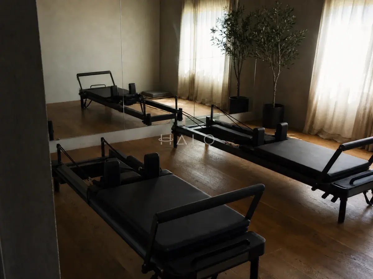 Reformer pilates studio with sheer drapery, planting and dark equipment on a stone floor