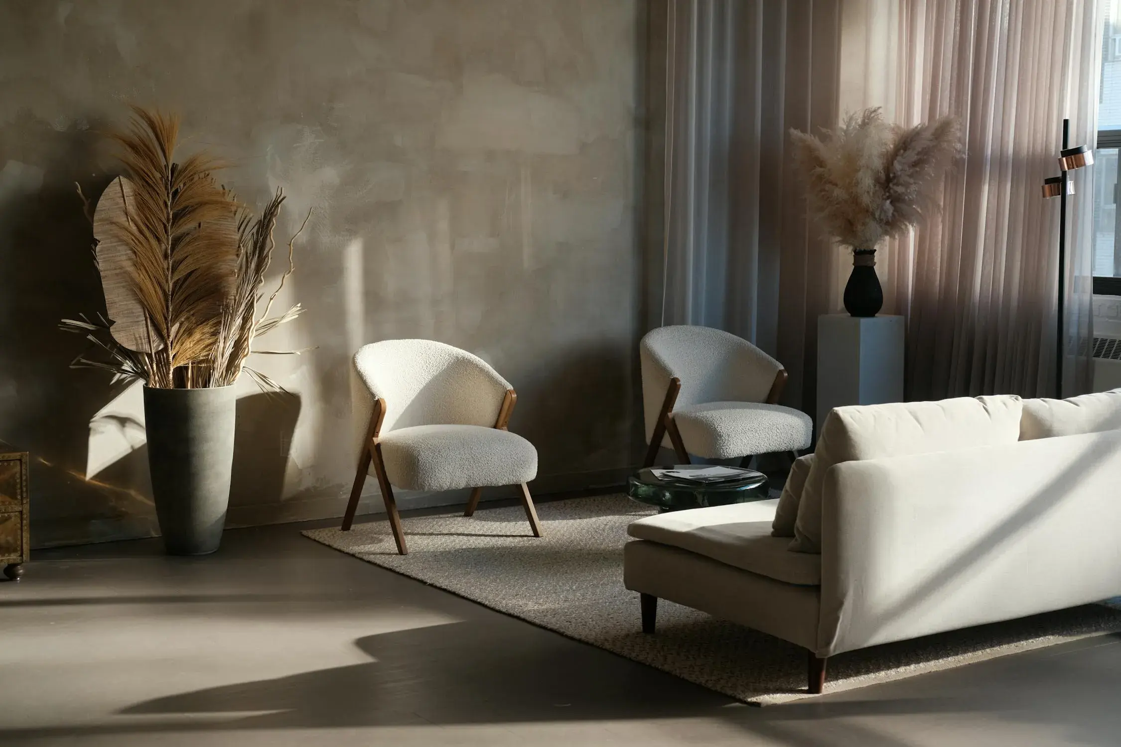 Japandi living room with a cross-laid limewash wall, bouclé chairs on timber frames and a seamless poured floor under raking daylight