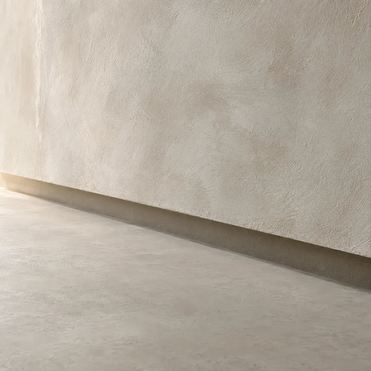 Close detail of a flush shadow gap where a limewashed plaster wall meets a seamless floor