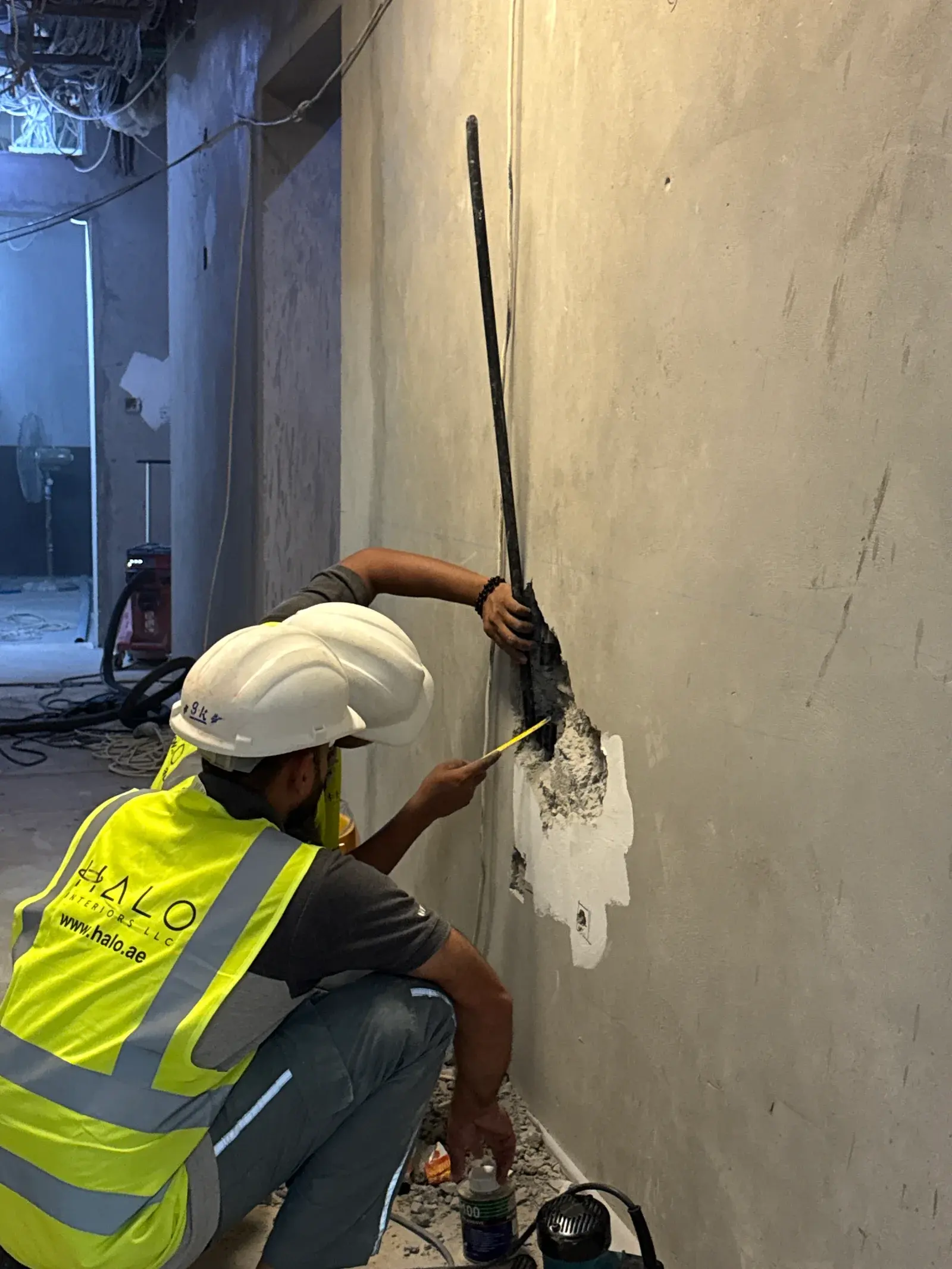 Halo operative in branded high-visibility PPE chasing a wall channel for conduit on a Dubai site