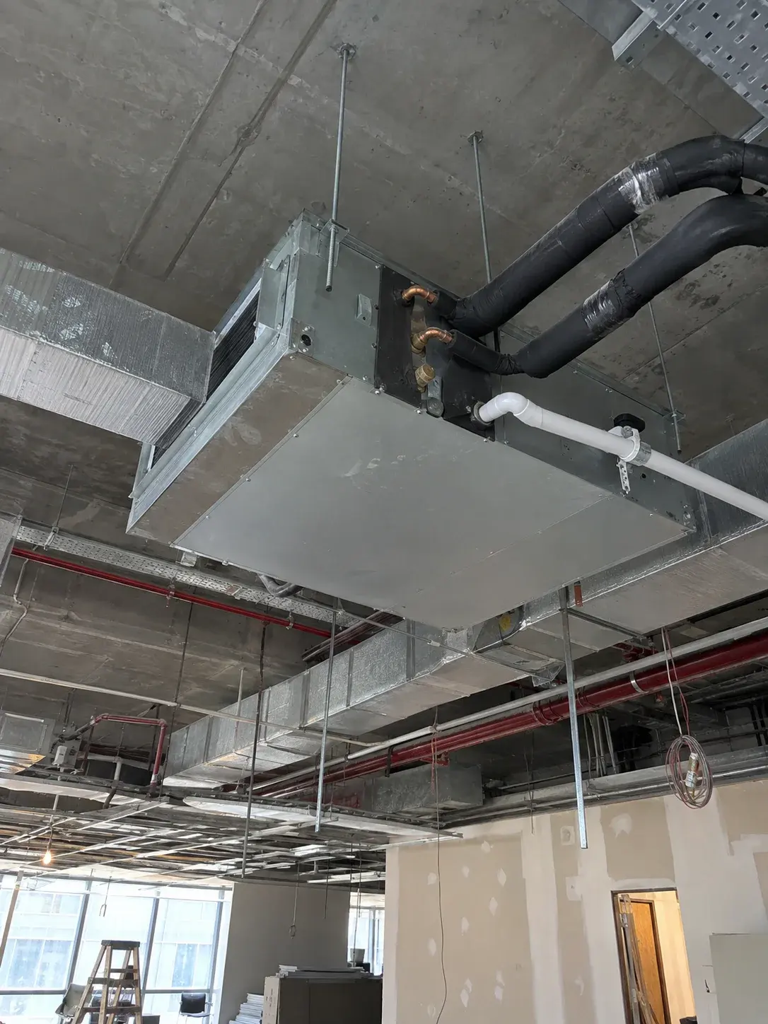 Concealed ducted fan coil unit with insulated refrigerant lines and condensate drain above an office ceiling