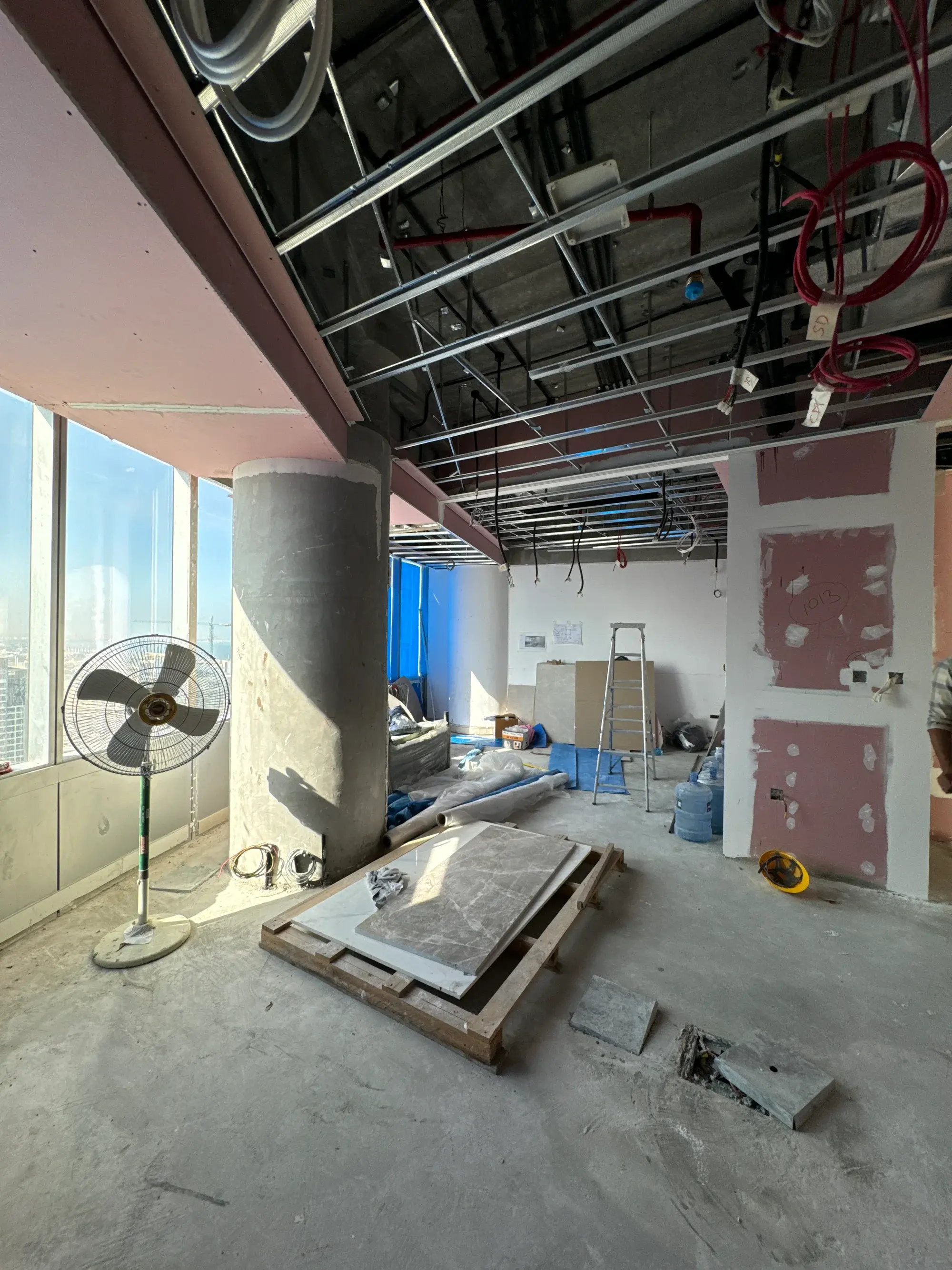 Open ceiling void in a Dubai tower with ductwork, cable containment and a red sprinkler main