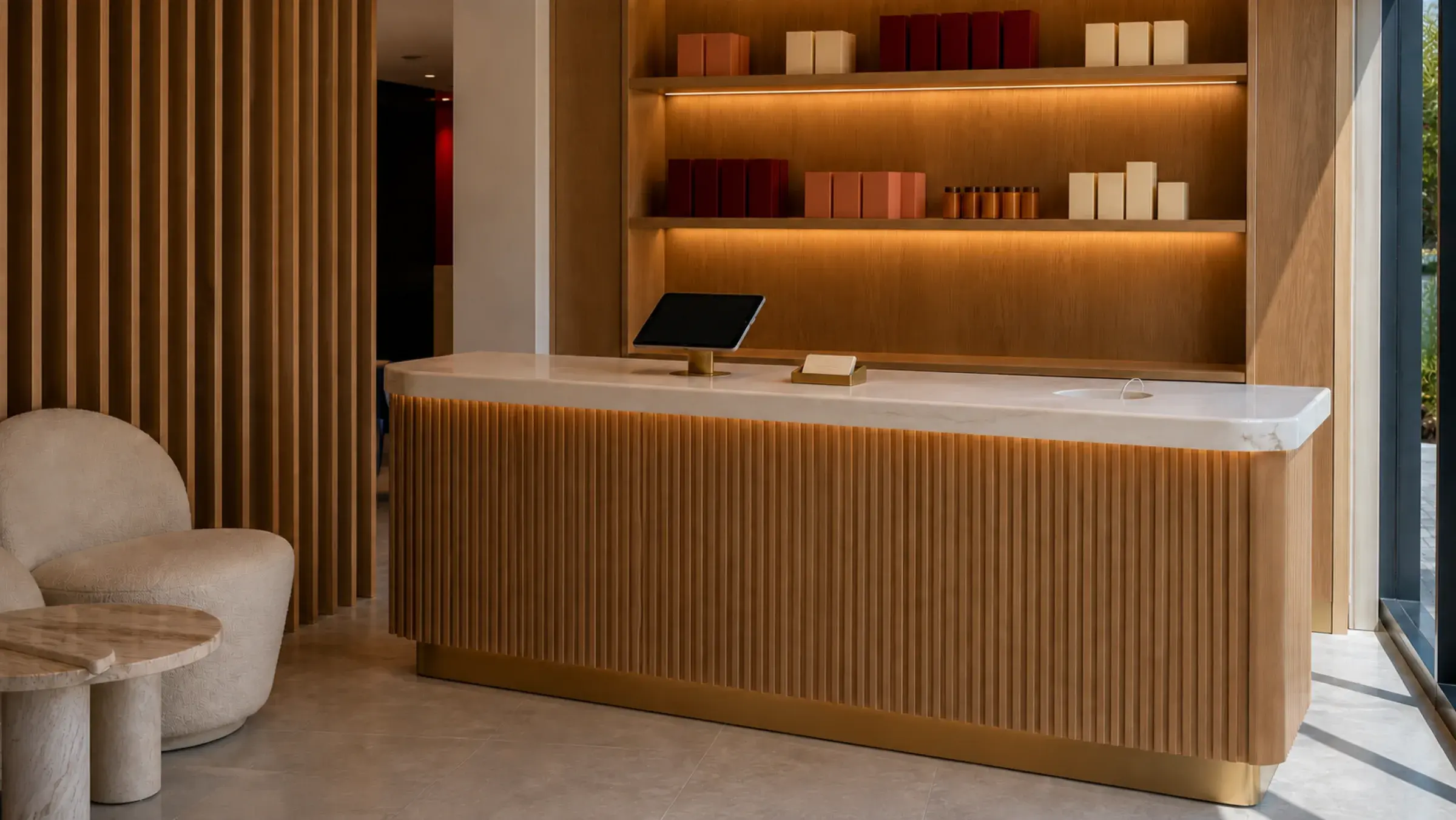 Fluted oak salon reception counter with a cream stone top, illuminated shelving and a waiting chair