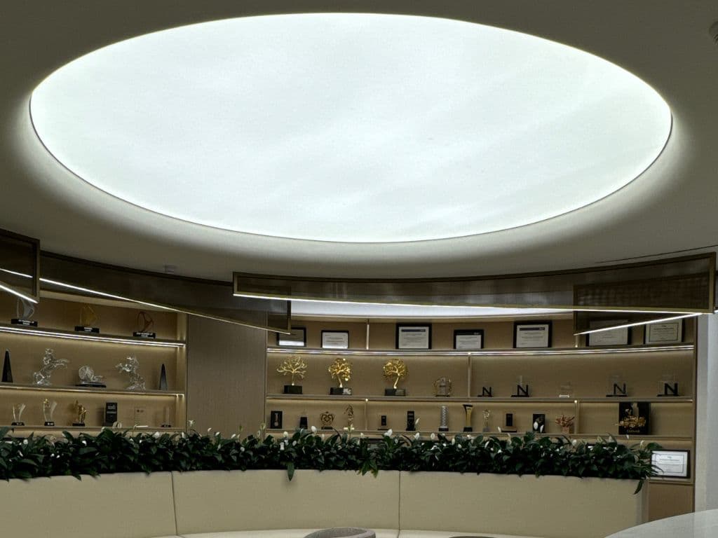 Circular backlit stretch ceiling above a display and award wall in a Dubai showroom